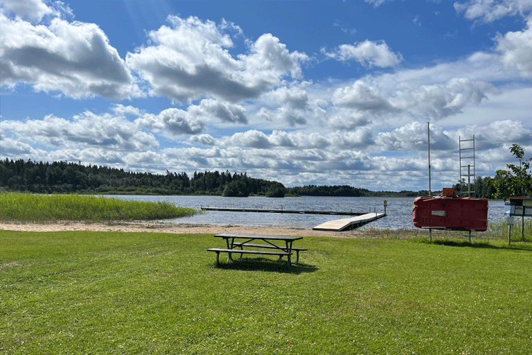 Badplatsen Stora Björkens med gräsmatta, sandstrand och en brygga.
