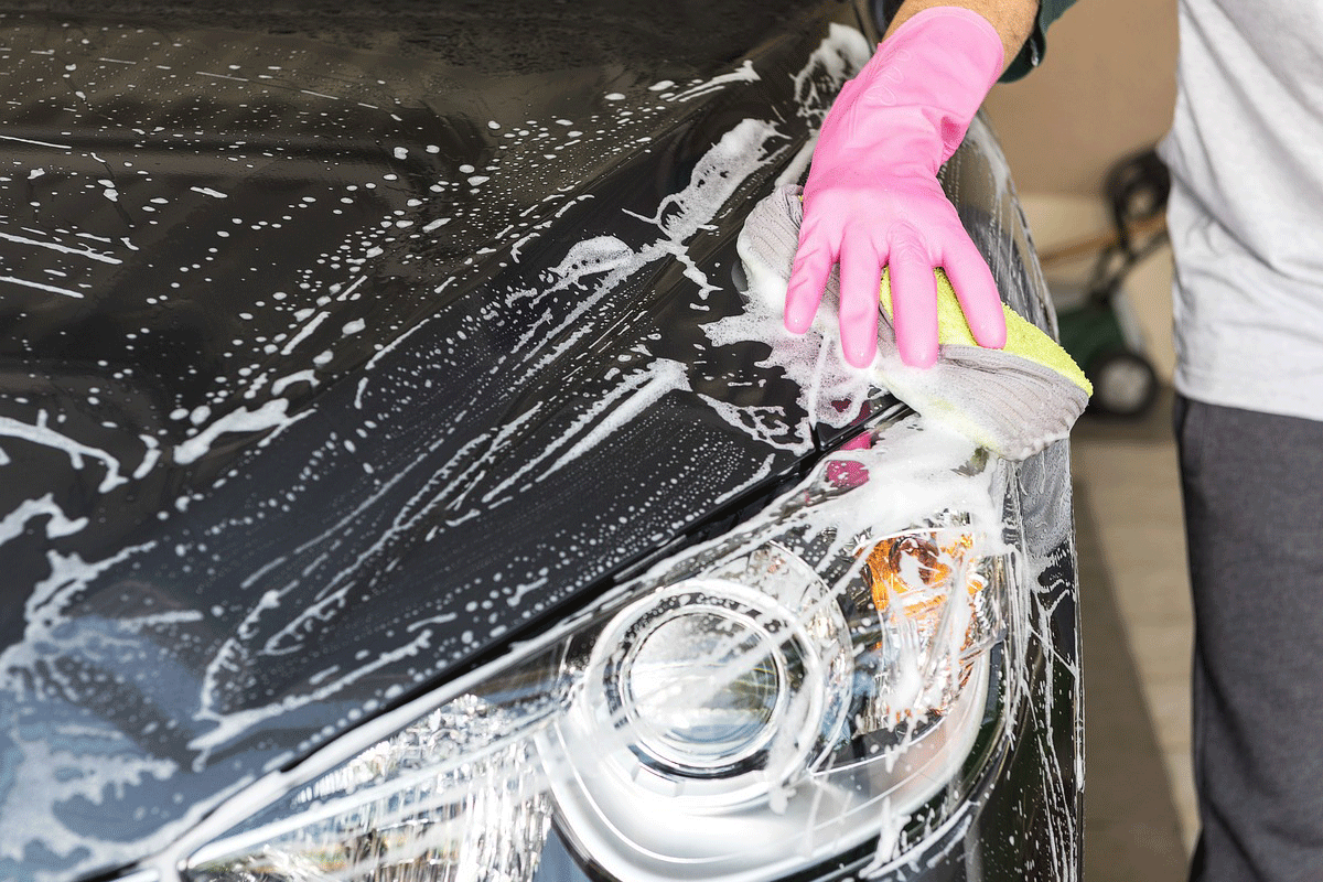 En hand med rosa plasthandske tvättar en motorhuv på en bil