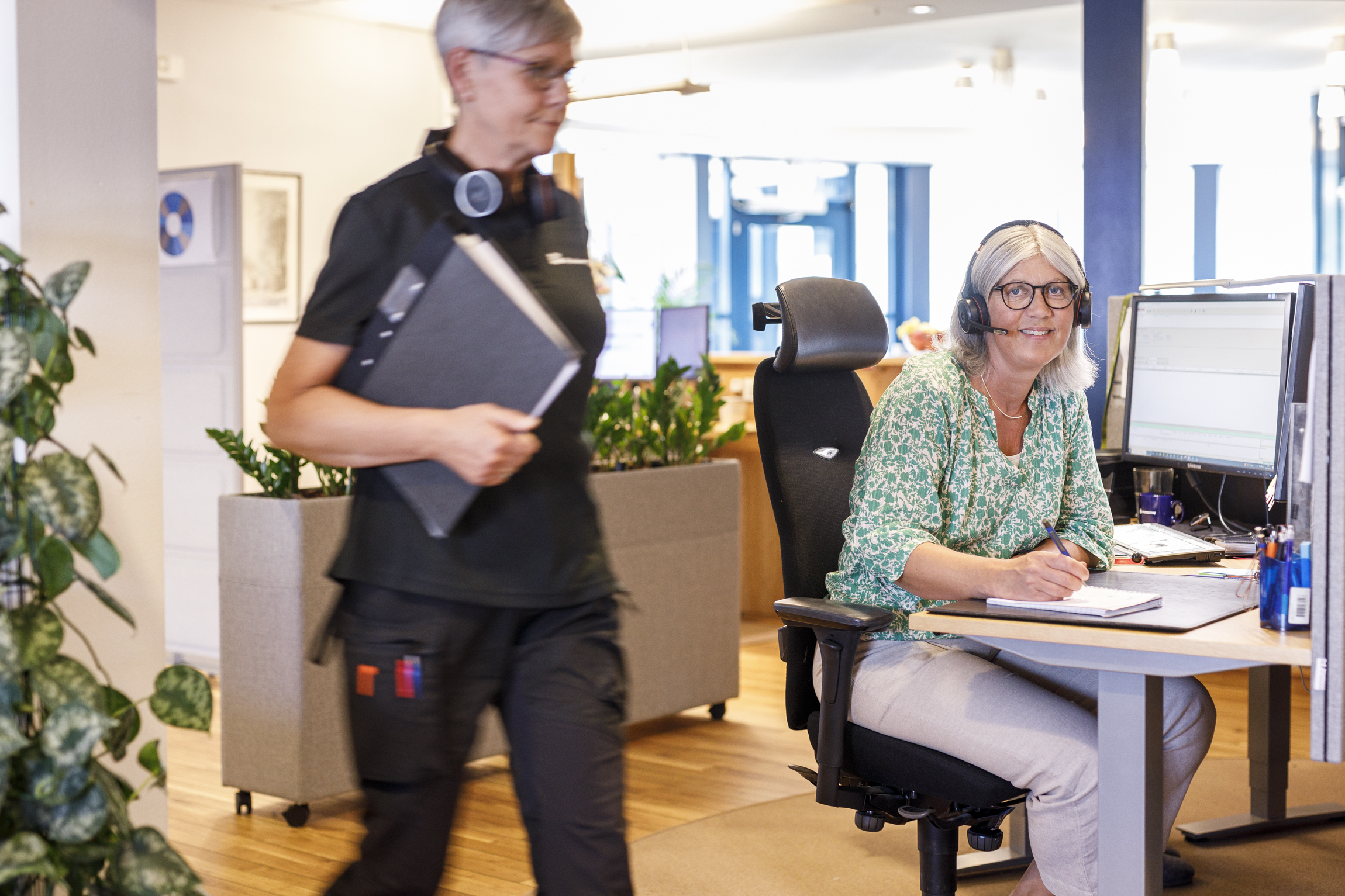 Två tjejer i kundservice. En håller i en pärm, den andra talar i ett headset.