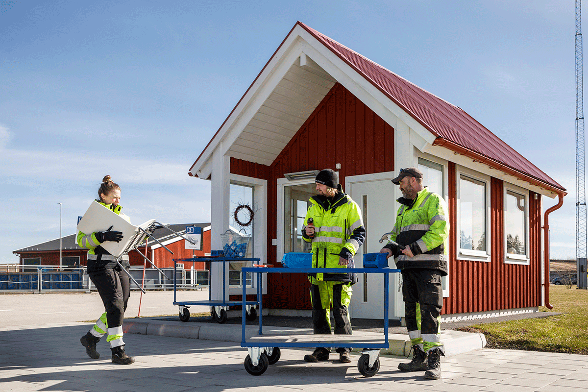 Tre personer i varselkläder demonterar avfall på en återvinningscentral