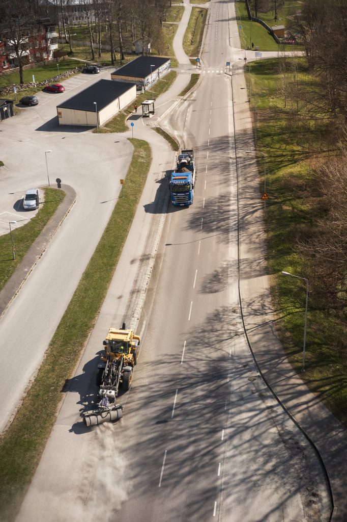 EE-UEAB-SopningGator-0102-high Lastmaskin som sopar grus på vägen och lastbil som samlar upp gruset efter på vägen.