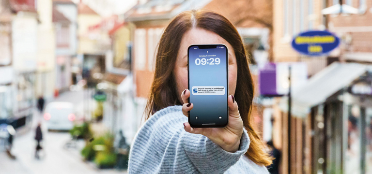 Annica_App En tjej håller en iPhone framför ansiktet. På skärmen visas en push-notis från Ulricehamns Energi.