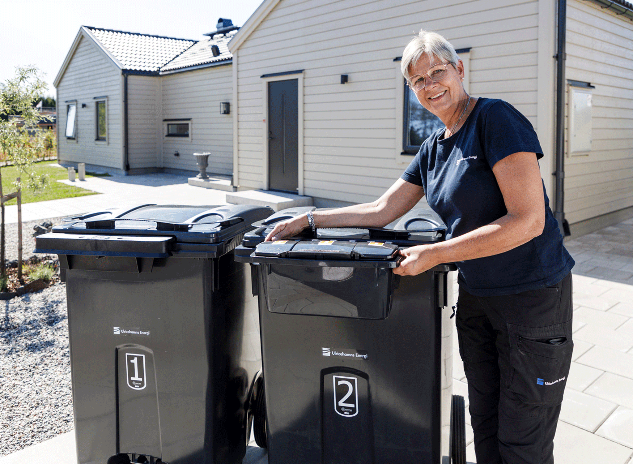 fyrfack En glad tjej står bredvid två svarta sopkärl.