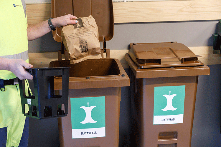 En hand slänger en papperspåse med matavfall i brunt kärl för matavfall