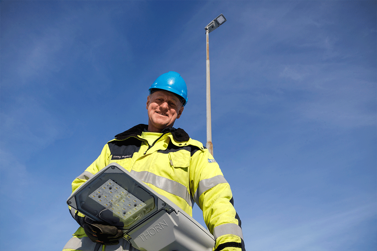 En man i varselkläder håller i en LED-armatur för gatljus.