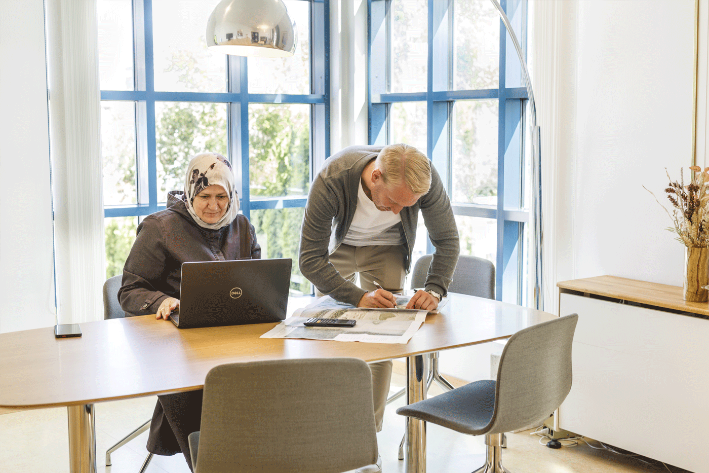 En kvinna och en man är vid ett konferensrum med en dator och lite ritningar.
