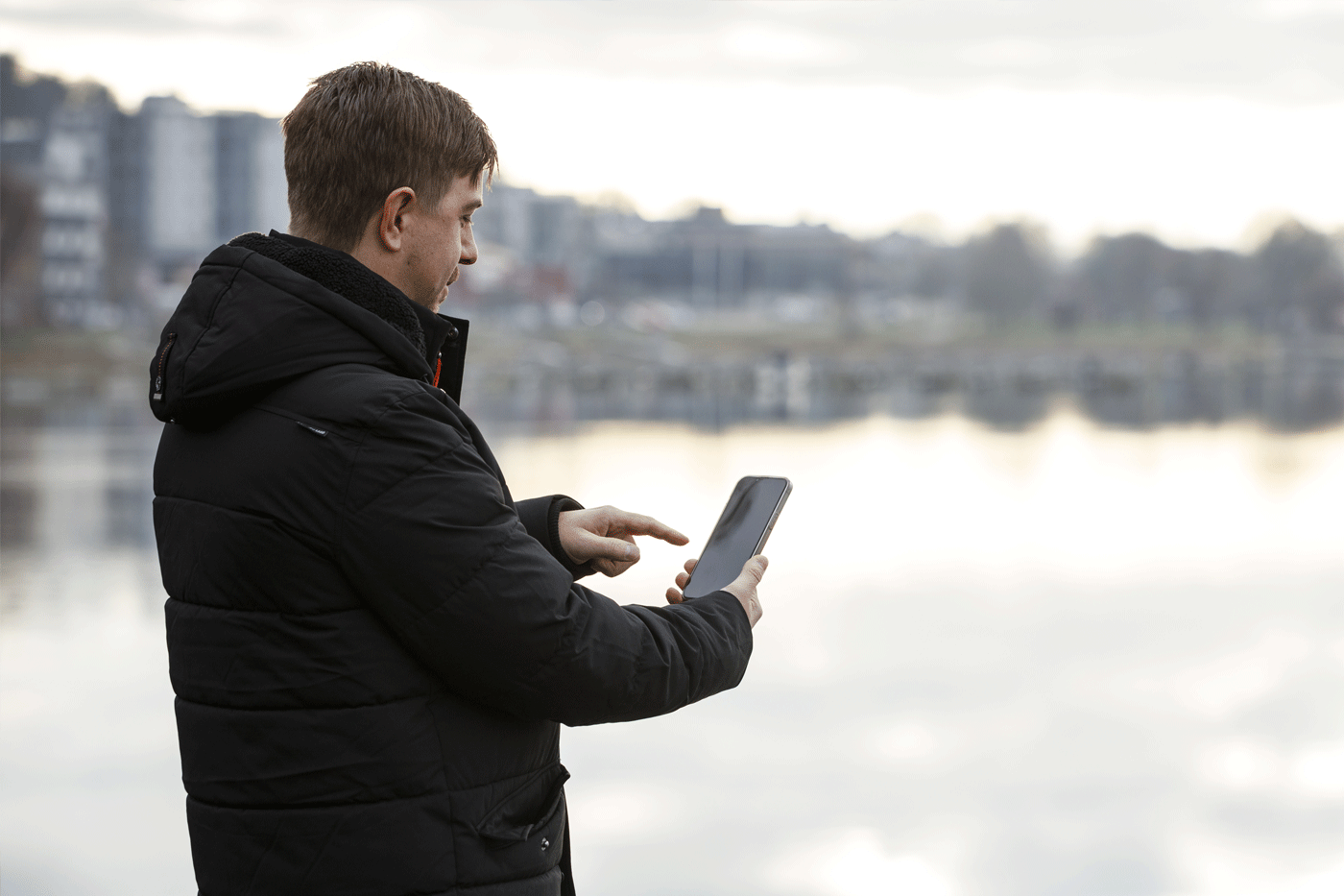En man står vid en strandkant med en mobiltelefon i handen. Han klickar på skärmen.