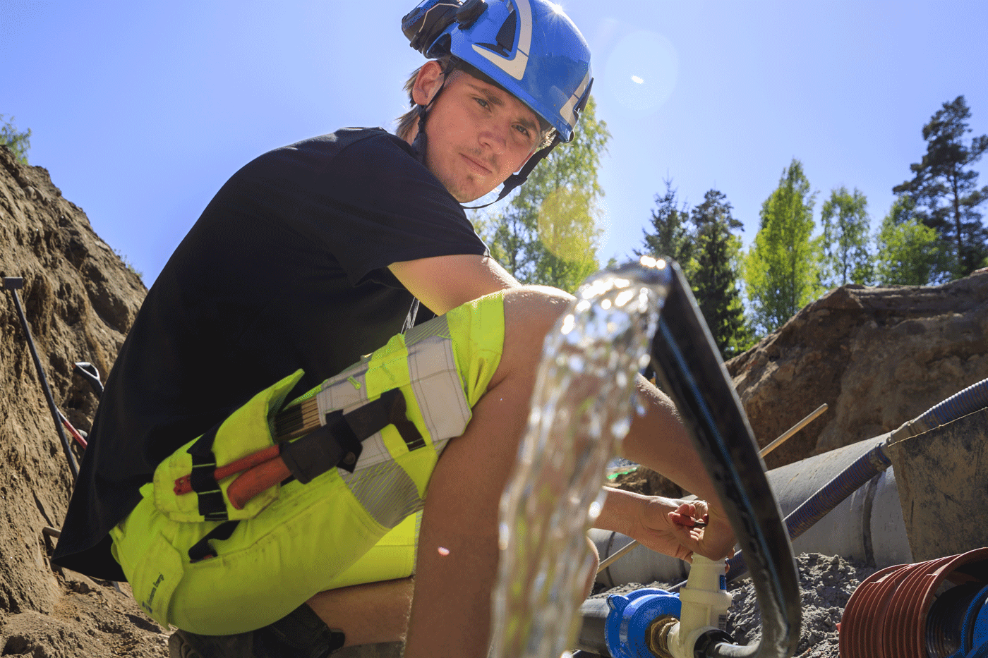 En man i varselkläder håller ett vattenrör där det rinner ut rent vatten