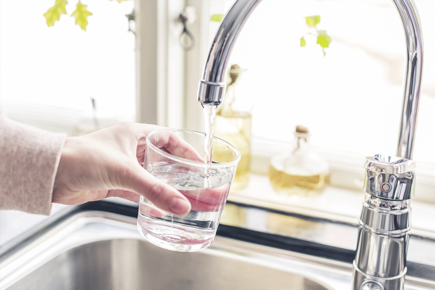 En hand håller i ett glas under en kran med rinnande vatten.
