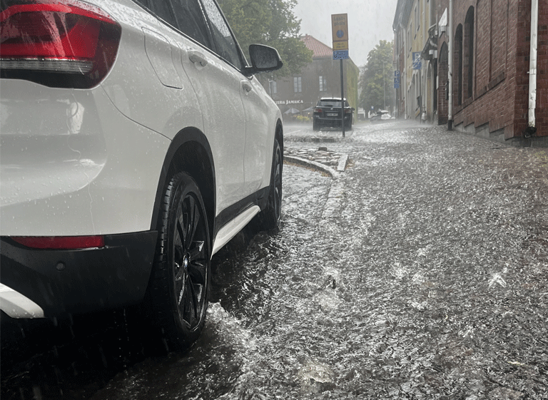 dagvatten En vit bil står parkerad längs en gata med forsande regnvatten