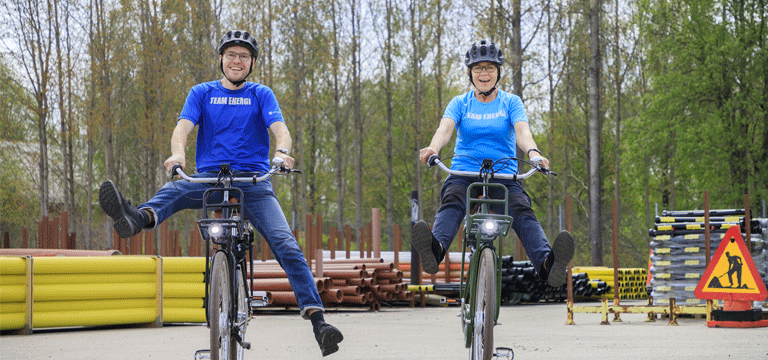 cyklar En man och en kvinna cyklar på varsin cykel. På en lagergård med plaströr i bakgrunden.
